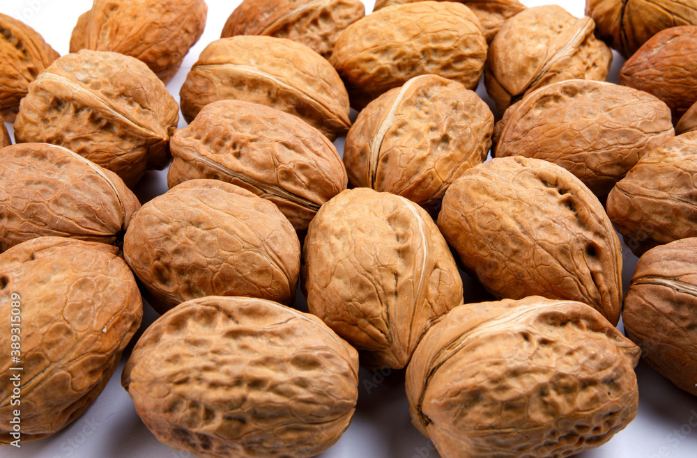 The background is formed by many whole walnuts on a white surface. The background is formed by many whole walnuts on a white surface.