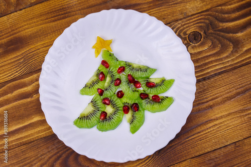 Christmas tree made of kiwi slices and pomegranate on wooden table. Top view. Creative idea for Christmas and New Year festive desserts. Funny food idea for kids