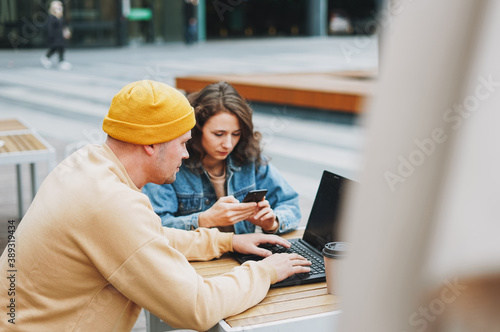 Stylish young couple freelancers working on laptop in the street cafe, woman using mobile