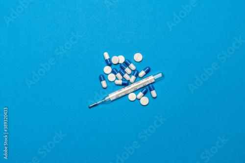 group of white pills or tablets and mercury thermometer on blue background