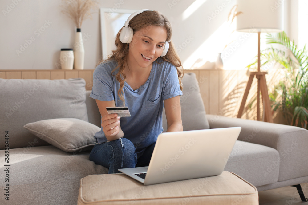 Happy natural blonde using credit card and laptop in the living room. Happy natural blonde using credit card and laptop in the living room.