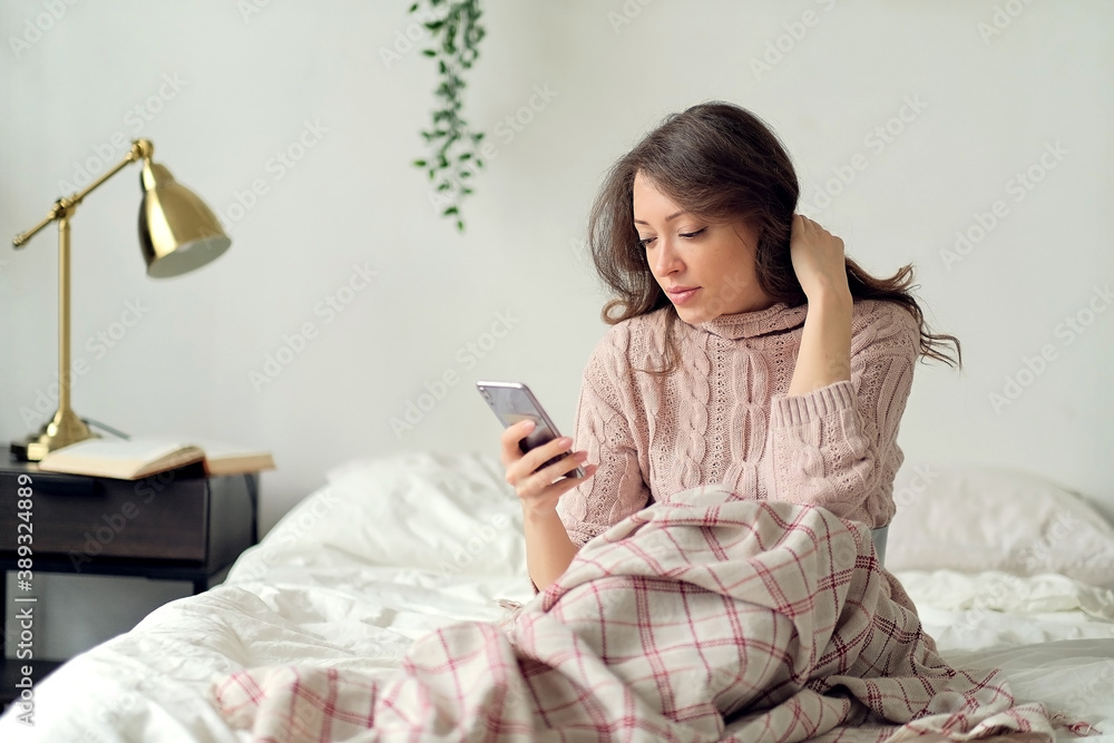 Careless, carefree young adult girl holding smartphone in hands, lying in bed, spending free time in bedroom and resting at morning. Careless, carefree young adult girl holding smartphone in hands, lying in bed, spending free time in bedroom and resting at morning.