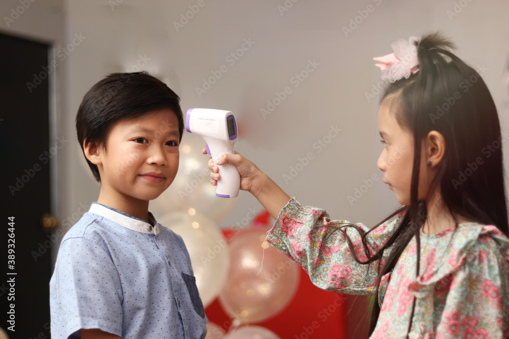 Girl holding digital medical electronic thermometer, measuring temperature for screening the boy at party event, prevent against infection of Covid-19 outbreak, new normal lifestyle
