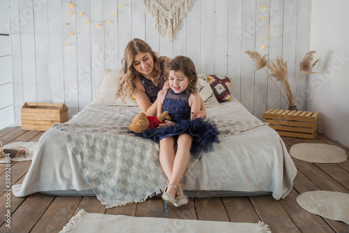 Mother and daughter in beautiful blue dress sittig on bed with teddy bear