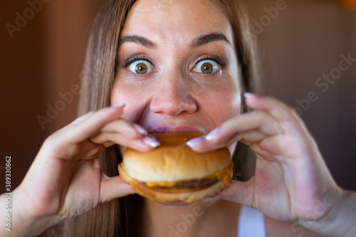 Close up of beautiful hungry young brunette is about to bite a delicious hamburger. Concept of junk food and fast food