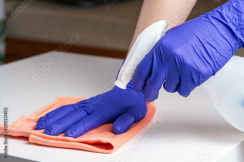 Young woman in medical purple gloves disinfecting the table surface with sanitizing antibacterial wipes. Protection against COVID-19. Concept of surface disinfection in hospitals and public places