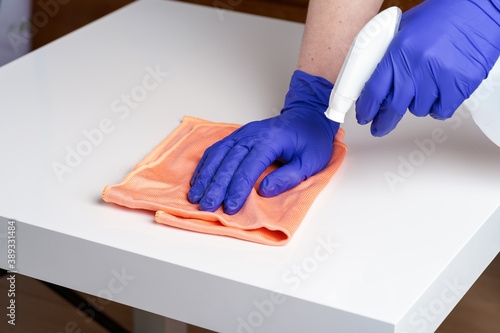 Young woman in medical purple gloves disinfecting the table surface with sanitizing antibacterial wipes. Protection against COVID-19. Concept of surface disinfection in hospitals and public places