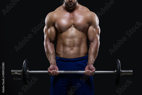 Handsome fitness man is standing with a heavy barbell ready to workout isolated on black background