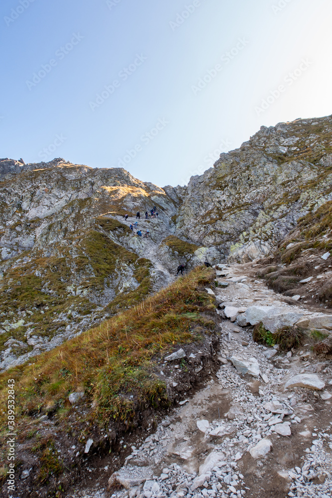 Many tourists climbing steep trail with chains towards Szpiglasowa Pass in Tatra Mountains, Poland, autumn.