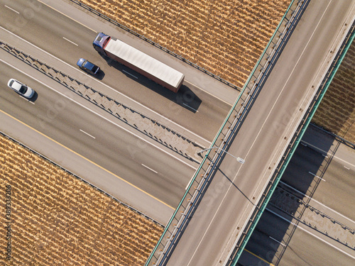 Dump truck carrying goods on the highway. Blue truck driving on asphalt road along the yellow fields. seen from the air.