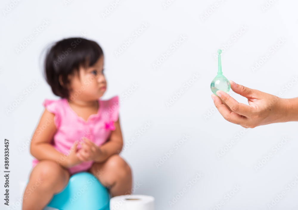 Asian little cute baby child girl training to sitting on blue chamber pot or potty her problem cannot shit and mother use Enema for help, studio shot isolated on white background, wc toilet concept Asian little cute baby child girl training to sitting on blue chamber pot or potty her problem cannot shit and mother use Enema for help, studio shot isolated on white background, wc toilet concept