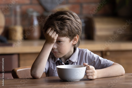 Bild auf Leinwand Unhappy small Caucasian boy child sit at kitchen table have no appetite for healthy breakfast