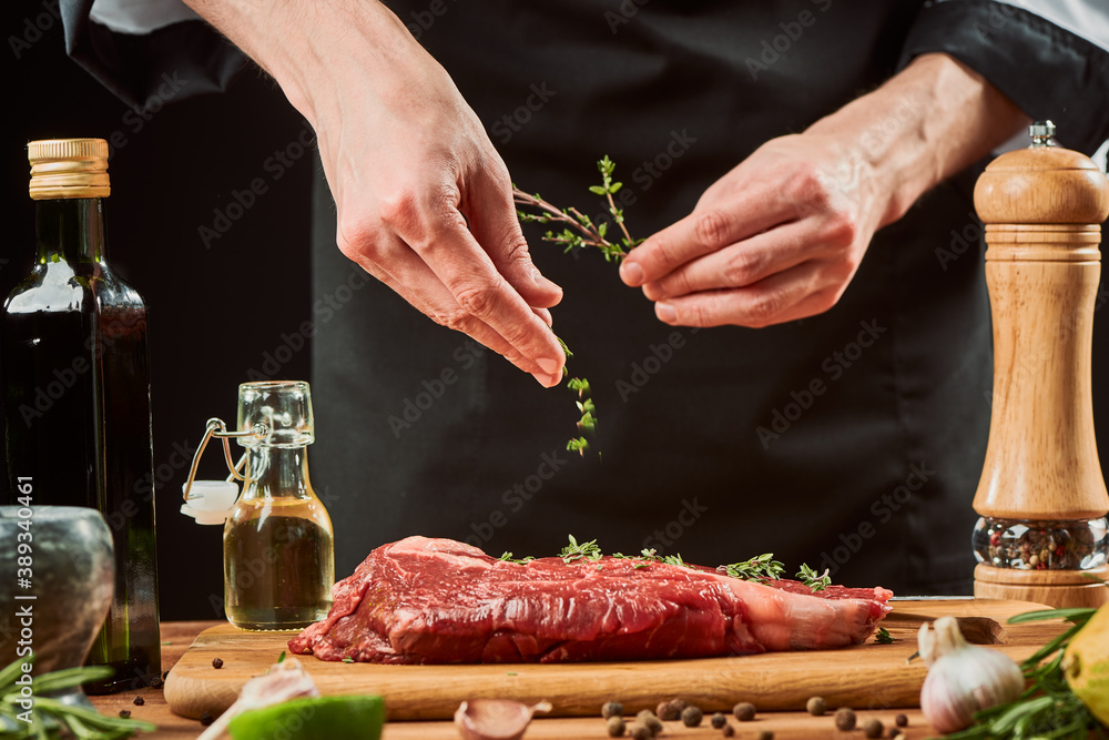 Chef throwing thyme leaves onto meat. Professional cook seasoning beef steak
