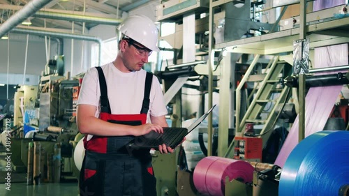 Male worker with a laptop is observing production of polyethylene foil