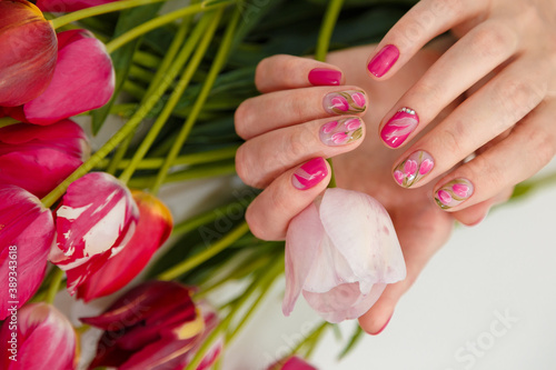 Female hands with tender spring manicure holding pink fresh tulip on flowers background. Nail art, gel nails polish design and beauty concept.