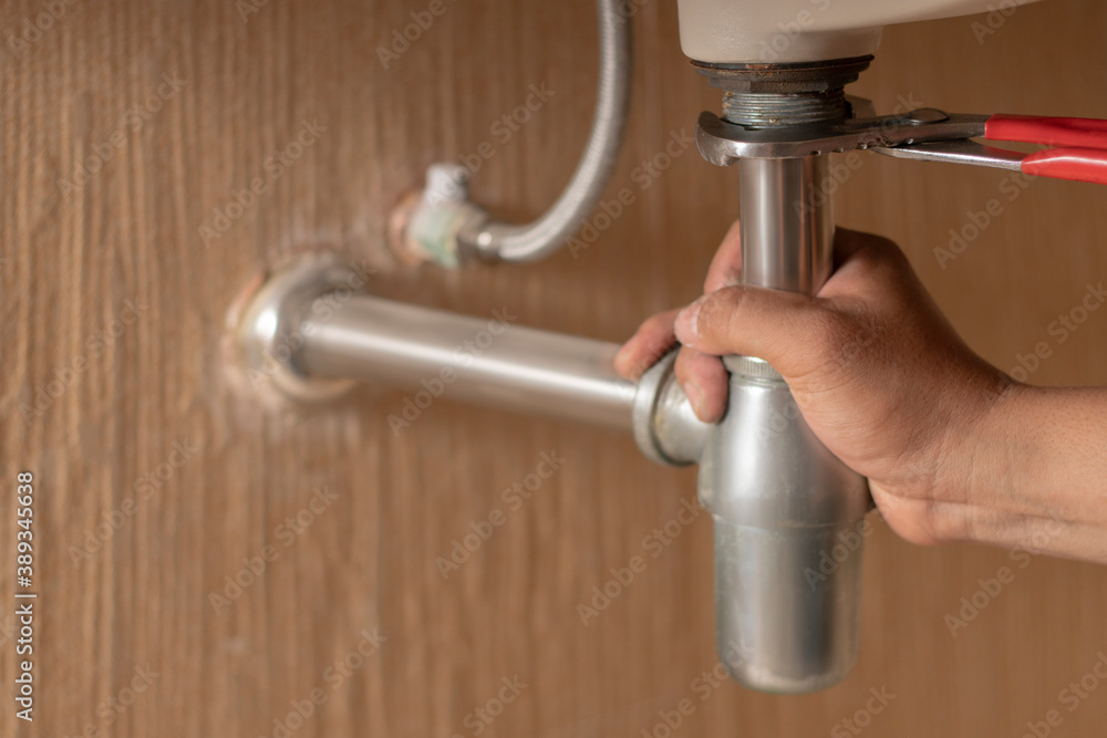 Plumber repairs and maintains chrome siphon under the washbasin in bathroom. Maintanance home ideas concept. Selective focus and freespace for background. Plumber repairs and maintains chrome siphon under the washbasin in bathroom. Maintanance home ideas concept. Selective focus and freespace for background.