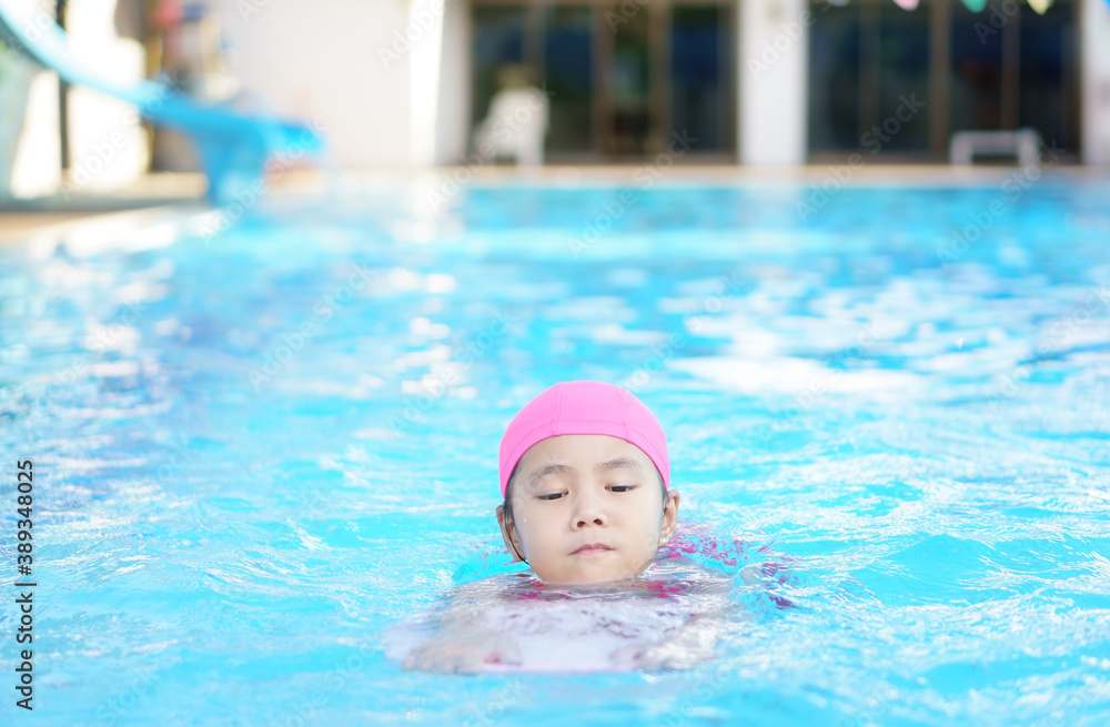 Asian child cute or kid girl wearing swimming suit on school swimming pool and happy fun in water park for learn and training swim on kick board or refreshing and relax to exercise on summer holiday