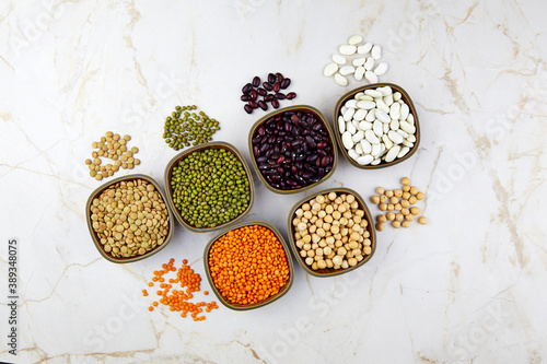 Legumes and beans assortment in bowls: lentils, beans, mung and chickpeas on light stone background. Top view, copy space. Healthy vegan protein food.