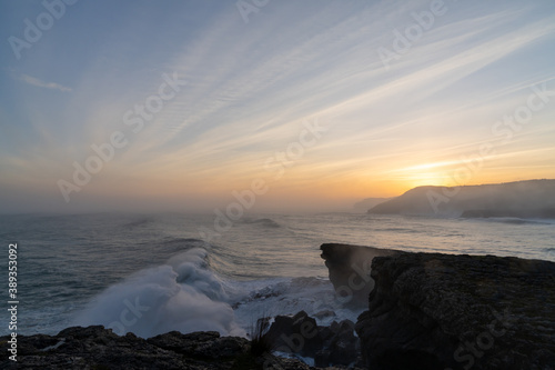 huge storm surge ocean waves crashing onto shore and cliffs at sunrise