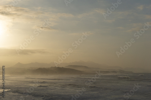 ocean coast at sunset with waves breaking and mountains in silhouette behind