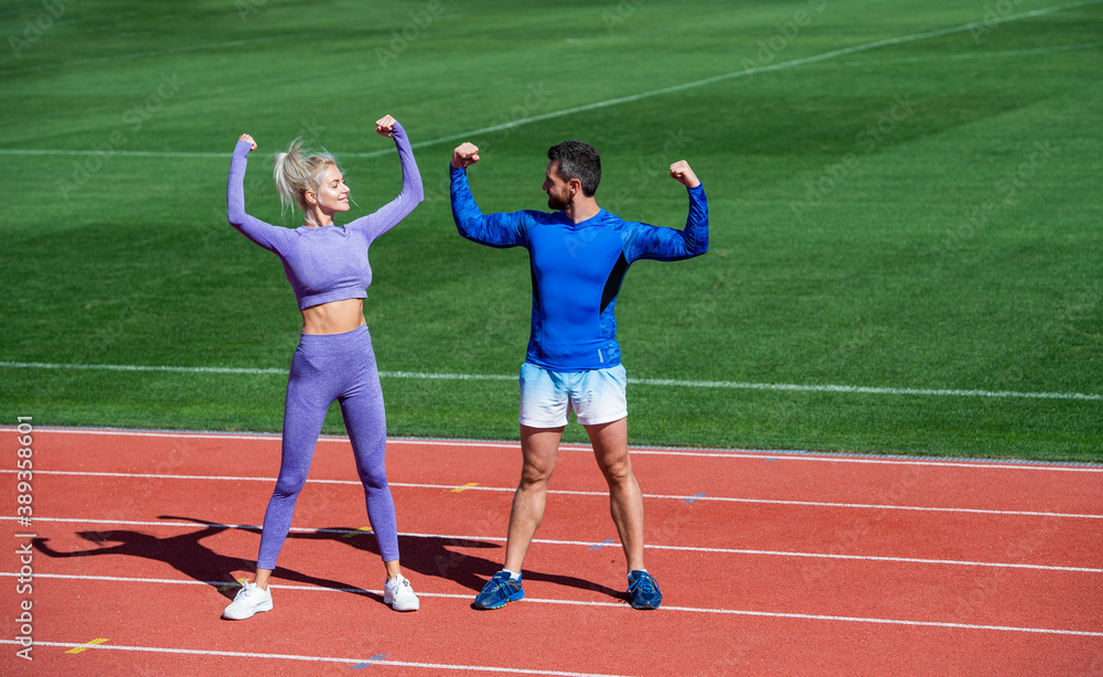 fitness woman and man celebrate success or show biceps muscles together on outdoor stadium racetrack wearing sportswear, sport success