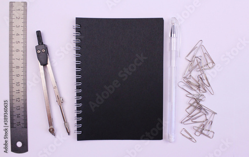 Black notepad for writing with compasses, ruler, paper clips and pencil on white background