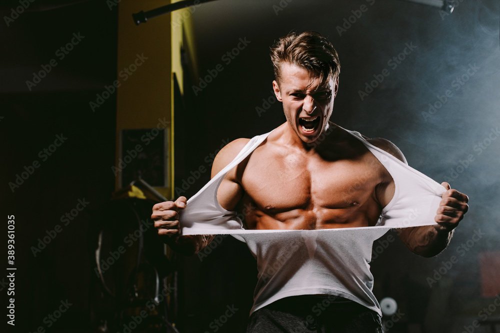 powerful man tearing shirt. Bodybuilder man pumping muscles and ripping shirt in gym. Hot and handsome man tearing shirt with anger and furious. Fitness motivation background