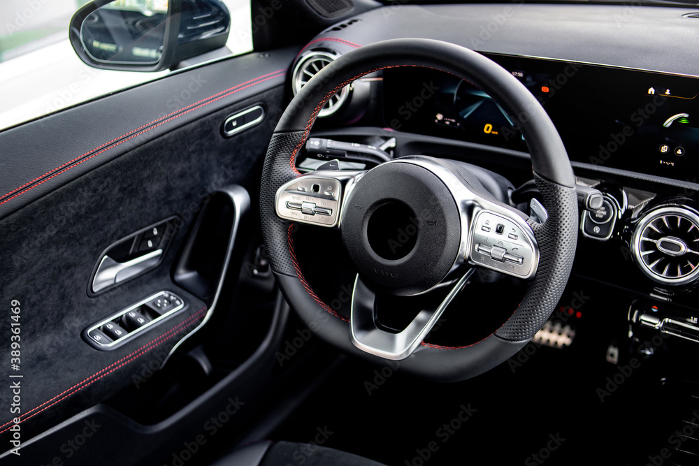 Close-up of the dashboard, speedometer, tachometer and steering wheel with phone setting and volume buttons. Luxurious car interior details.