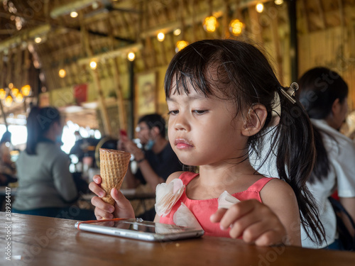 A girl wearing a hearing aid  Eating ice-cream and watch cartoons on the smart phone