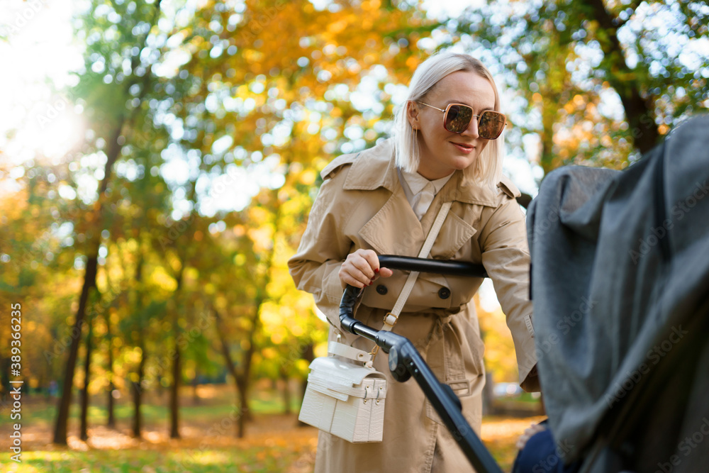 Mother with baby pram walking in autumn park Mother with baby pram walking in autumn park