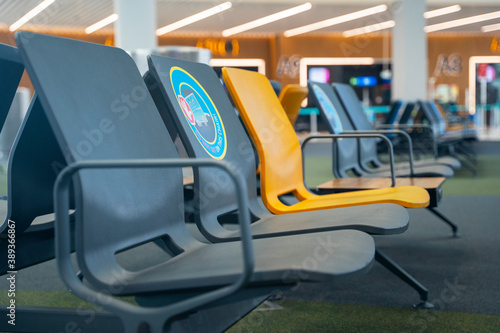 Row of multicolored plastic seats on carpet in airport waiting room, with a social distance warning sticker, close up, blurred background. Facilities for passengers before or between departures.