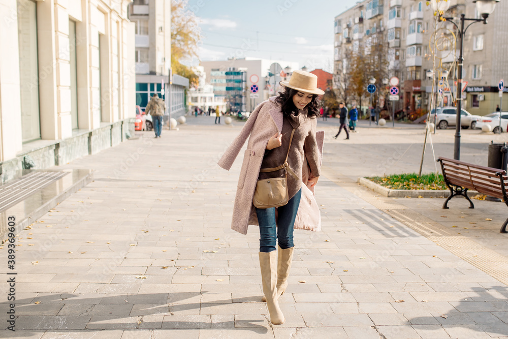beautiful caucasian brunette woman in a stylish outfit walking down the street in the offseason in a coat and hat
