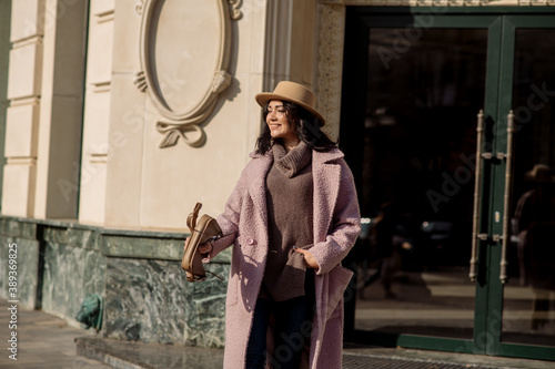 beautiful caucasian brunette woman in a stylish outfit walking down the street in the offseason in a coat and hat 