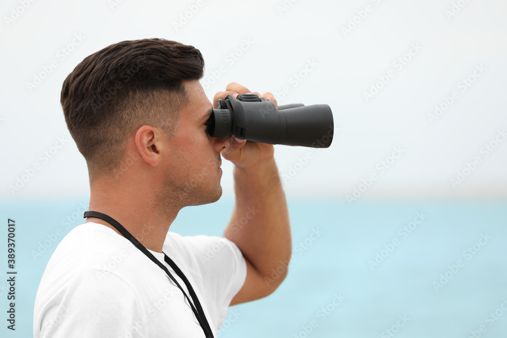 Obraz premium Handsome male lifeguard with binocular near sea