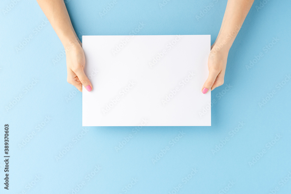 Young female hands showing empty white paper sheet on blue background. Mockup Young female hands showing empty white paper sheet on blue background. Mockup