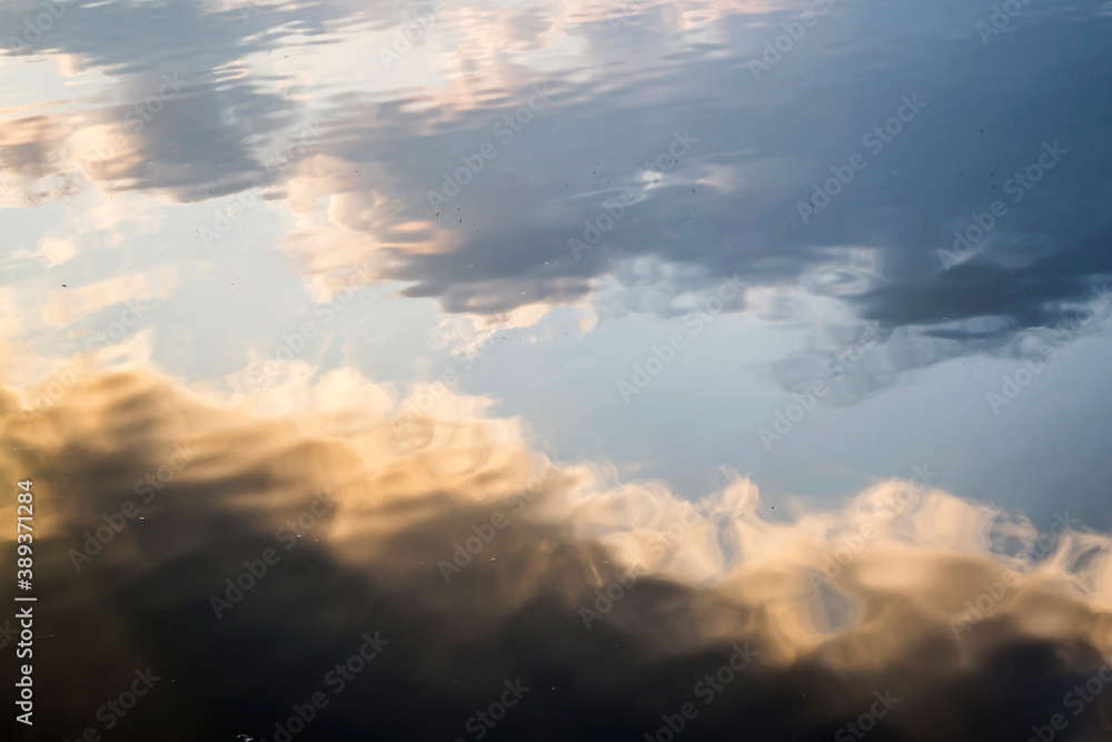 Water background where the sky is reflected with the sunset and clouds, like a gradient.