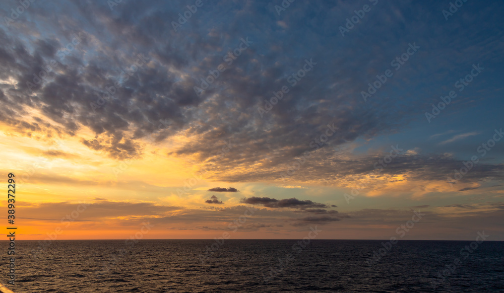 Sunset and dramatic set of clouds drifting over the tropical waters of the Caribbean Sea are lit by the last moments of daylight.