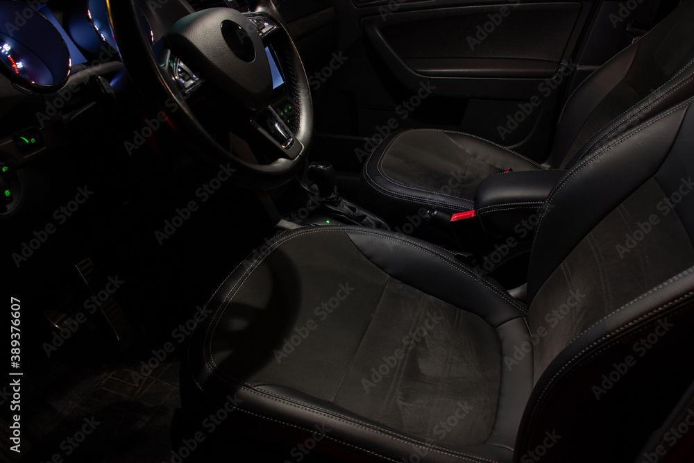 The driver's seat in the cabin of a modern car with a leather steering wheel and expensive equipment. Night photography with interior lighting