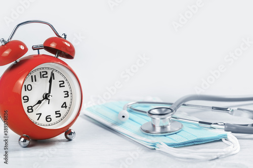 Medical or healthcare concept banner. Red alarm clock with stethoscope on top of of medical face mask. Doctor appointment or checkups schedule. Copy space.