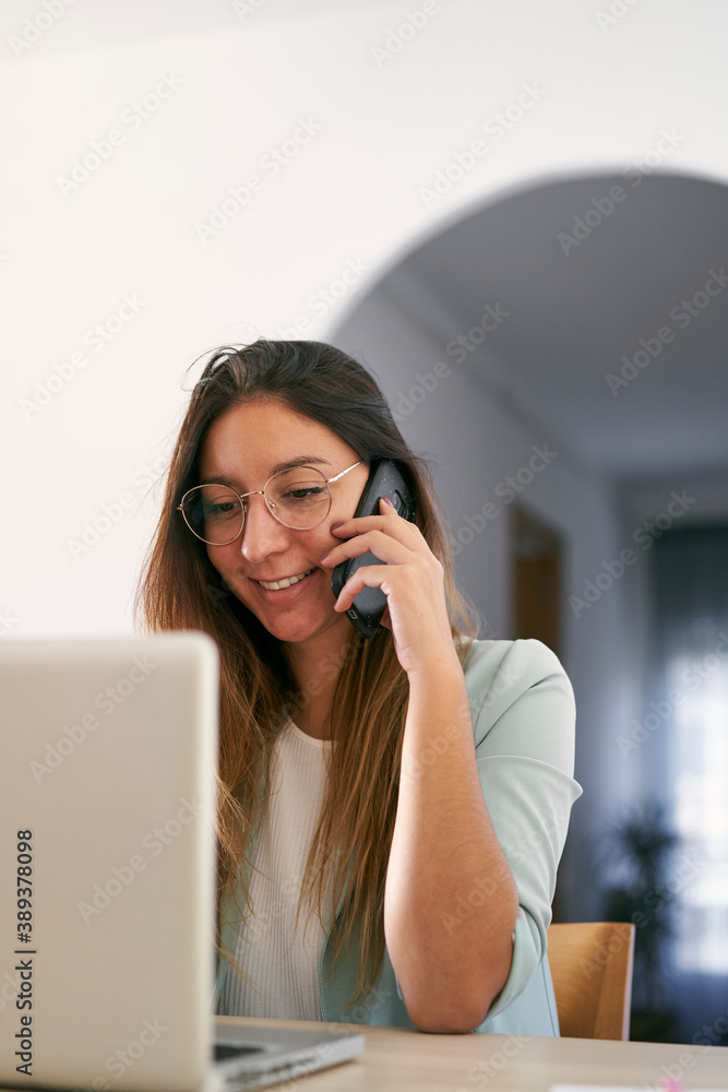 Front view of a smiling woman working at home with laptop and talking on the phone. Vertical photo. Front view of a smiling woman working at home with laptop and talking on the phone. Vertical photo.