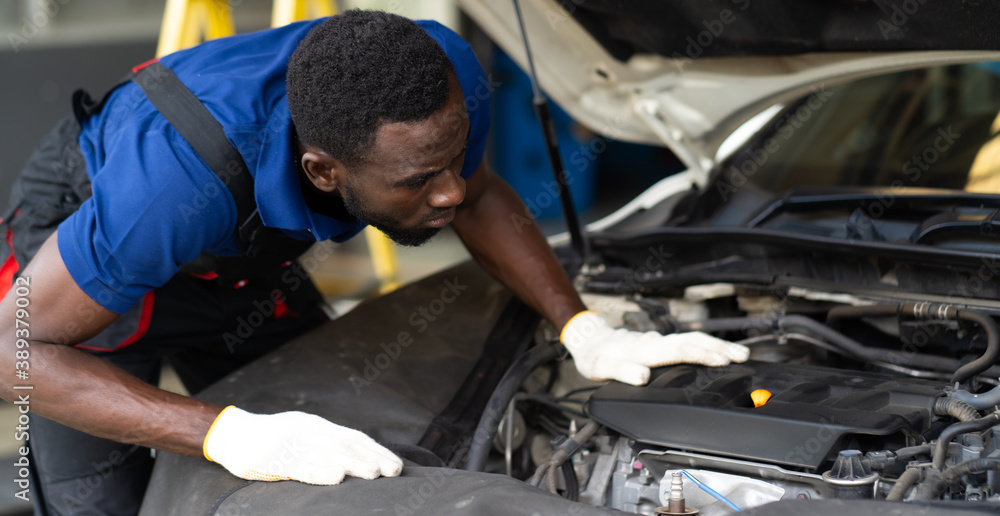 Black male mechanic repairs car in garage. Car maintenance and auto service garage concept. Black male mechanic repairs car in garage. Car maintenance and auto service garage concept.