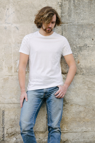 Hipster handsome male model wearing white blank t-shirt with space for your logo or design in casual urban style on europian streets