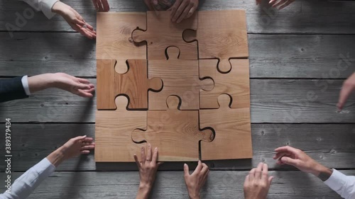 Business people team sitting around meeting table and assembling wooden jigsaw puzzle pieces unity cooperation ideas concept