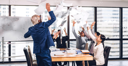 Successful group of casual business relaxing and throwing paper in modern work loft.Creative business people celebrating with arms up.Teamwork and success concept