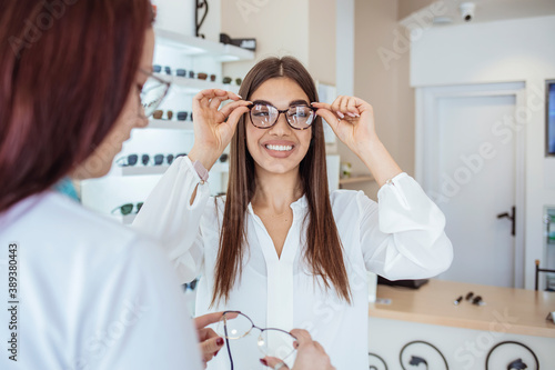 Young smiling woman is trying on eyeglasses in optical shop with the assistance of optometrist. Woman trying on eyeglasses in optical shop. Joyful happy woman trying some eyeglasses