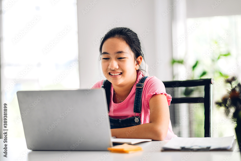 School kid little girl learning and looking at laptop computer making homework studying knowledge with online education e-learning system.children video conference with teacher tutor at home School kid little girl learning and looking at laptop computer making homework studying knowledge with online education e-learning system.children video conference with teacher tutor at home