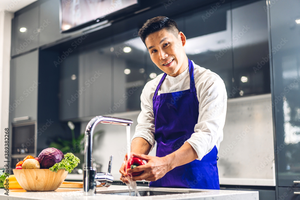 Portrait of smiling professional handsome asian man chef cooking and preparing salad with cooked food on counter standing in the restaurant commercial kitchen Portrait of smiling professional handsome asian man chef cooking and preparing salad with cooked food on counter standing in the restaurant commercial kitchen