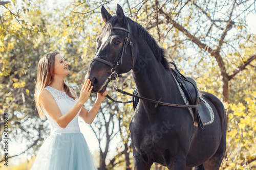 woman in white wedding dress walking with a horse in autumn park