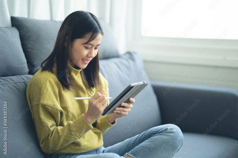 An Asian woman sitting on a tablet on a sofa An Asian woman sitting on a tablet on a sofa