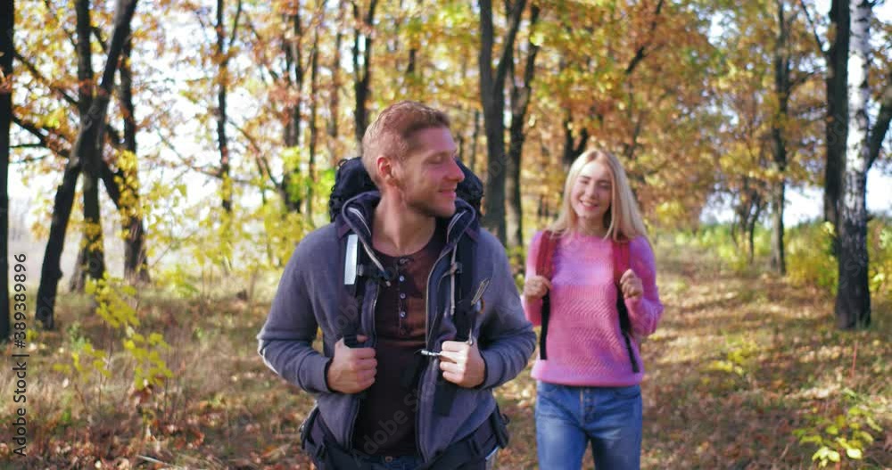 On sunny afternoon, couple walks through autumn forest. Young guy with backpack on his back looking to sides turns back. Light-willed girl with backpack has walk. Tourists. High quality 4k footage On sunny afternoon, couple walks through autumn forest. Young guy with backpack on his back looking to sides turns back. Light-willed girl with backpack has walk. Tourists. High quality 4k footage
